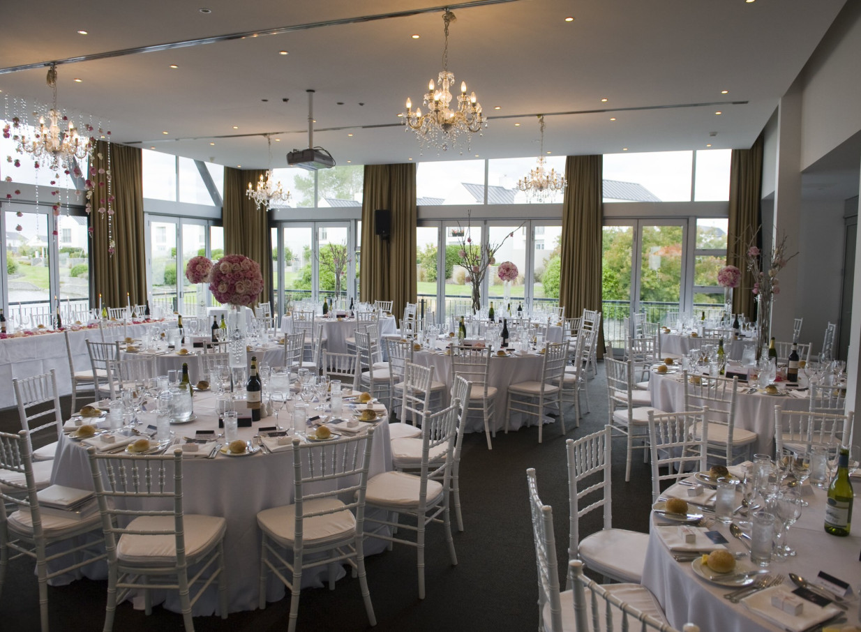 An elegant modern reception room at Peppers Clearwater, Christchurch, features floor-to-ceiling windows overlooking a serene golf course and lake.