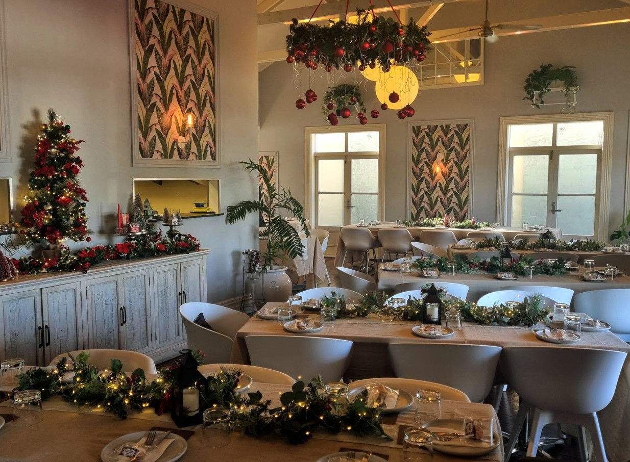 A festive dining room in Moxie, a charming Auckland villa, features tables adorned with garlands and lights.