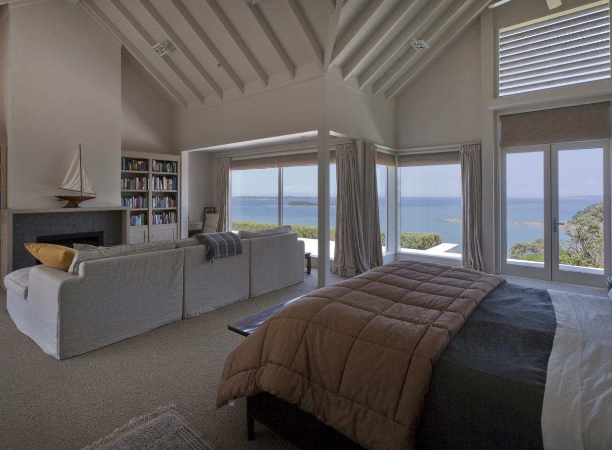 This luxurious bedroom and living space at Tu Ngutu Villa, Auckland, boasts vaulted ceilings and expansive coastal views.