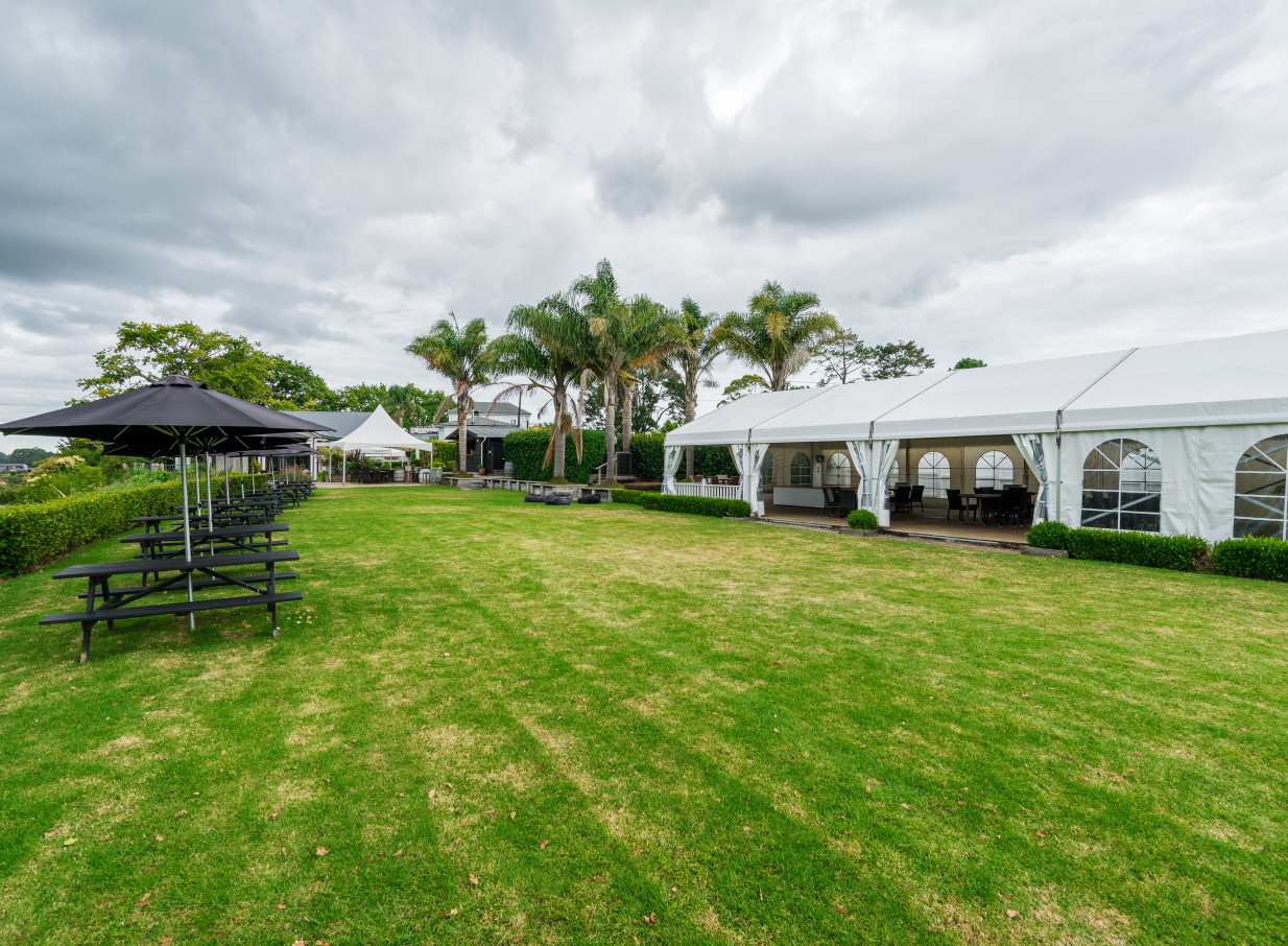 The Boat House, a scenic riverside venue in Auckland, features an expansive outdoor lawn with a permanent marquee and picnic seating.