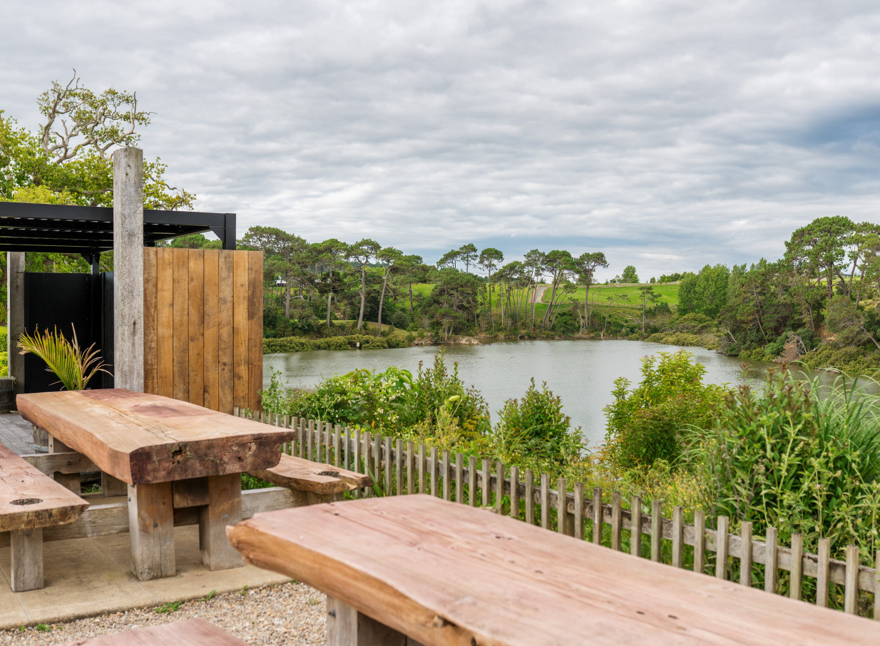 An outdoor dining area at The Boat House in Auckland, featuring rustic wooden tables overlooking a picturesque waterfront.