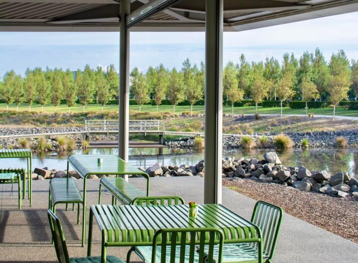 PERCY, Auckland, features a modern outdoor dining patio with green furniture, overlooking a tranquil pond and trees.
