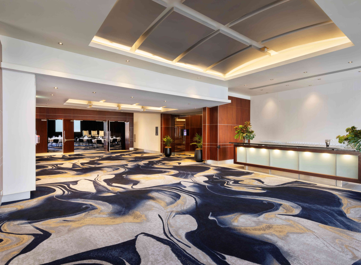 A sophisticated pre-function area with a modern abstract carpet and bar at Pullman Auckland Hotel & Apartments.