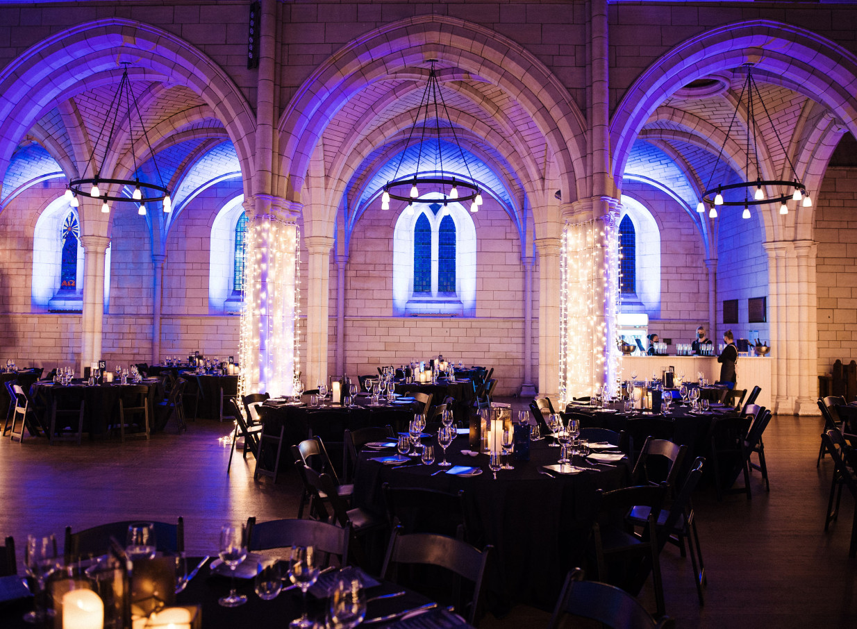 St Matthew-in-the-City, Auckland's neo-Gothic venue, hosts an elegant banquet setup bathed in atmospheric lighting.