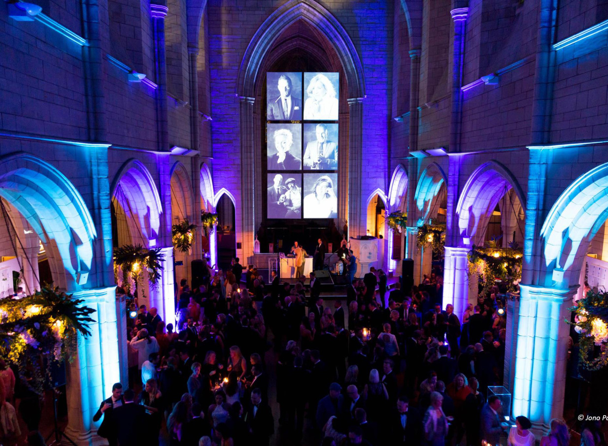 A lively reception fills the neo-Gothic church interior of St Matthew-in-the-City, Auckland, highlighted by vibrant blue and purple lighting.