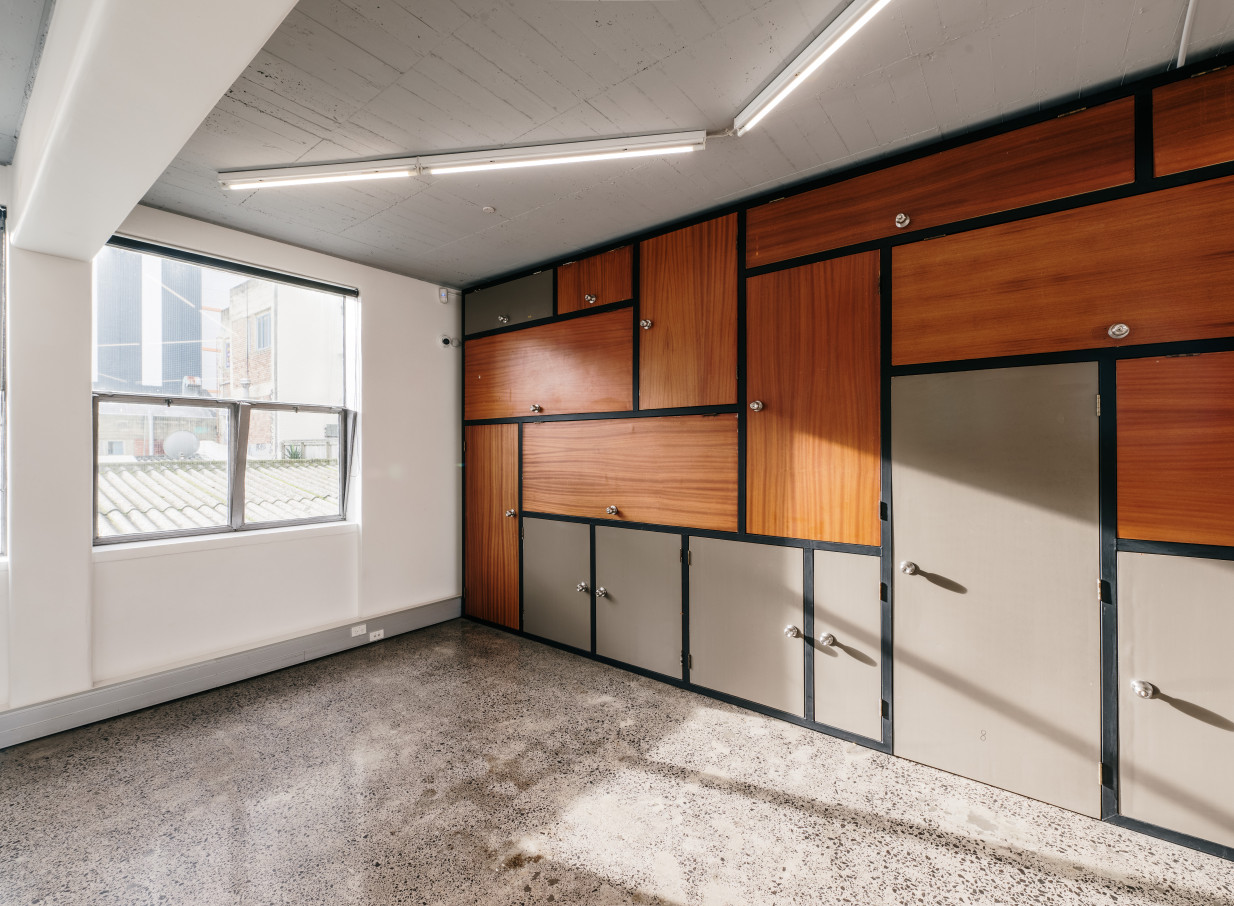 An industrial-chic room at The Tuesday Club, Auckland, showcases a large window and a modular wooden storage wall.