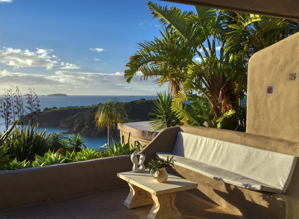 An outdoor patio with curved Mediterranean-inspired architecture at Delamore Lodge, Waiheke Island, overlooking Owhanake Bay.