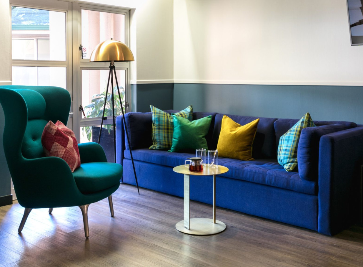 A cozy seating area with a vibrant blue sofa and teal armchair in the bold and eclectic boutique style of Naumi Auckland Airport.