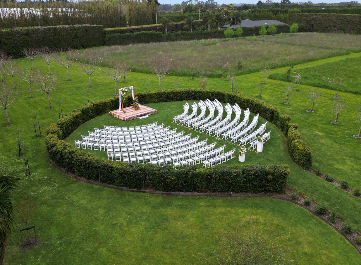 An outdoor wedding ceremony setup with white chairs in the manicured garden of Markovina Vineyard Estate in Auckland.