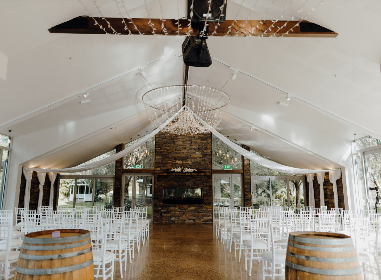 The elegant indoor ceremony space at Markovina Vineyard Estate, Auckland, features a schist fireplace and a delicate fairy light chandelier.
