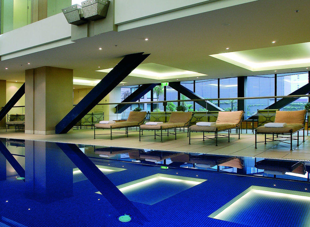 Grand Millennium Auckland's chic, modern indoor pool area features floor-to-ceiling windows and comfortable lounge chairs.