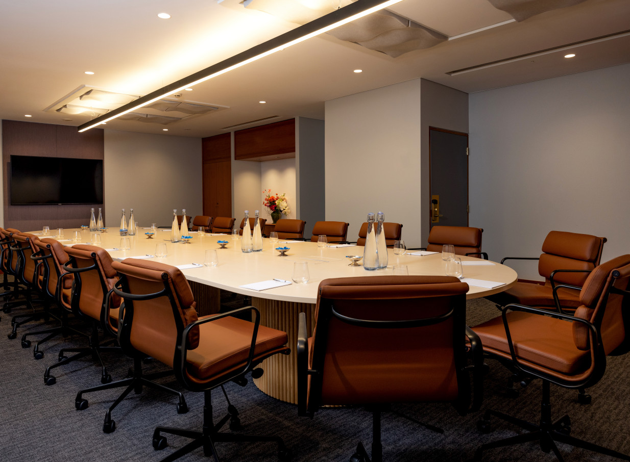 The chic, modern boardroom at Grand Millennium Auckland, featuring a large light-toned table and brown leather chairs.