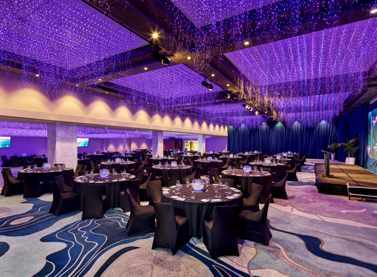 Grand Millennium Auckland's elegant ballroom features a banquet setup beneath an enchanting purple Sky Garden lighting sculpture.