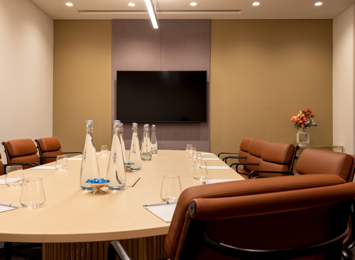 A modern and elegant boardroom meeting setup at Grand Millennium Auckland, featuring an oval table and brown leather chairs.