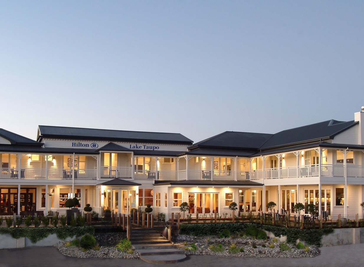 The Victorian-style heritage exterior of Hilton Lake Taupo features illuminated balconies and inviting outdoor dining.