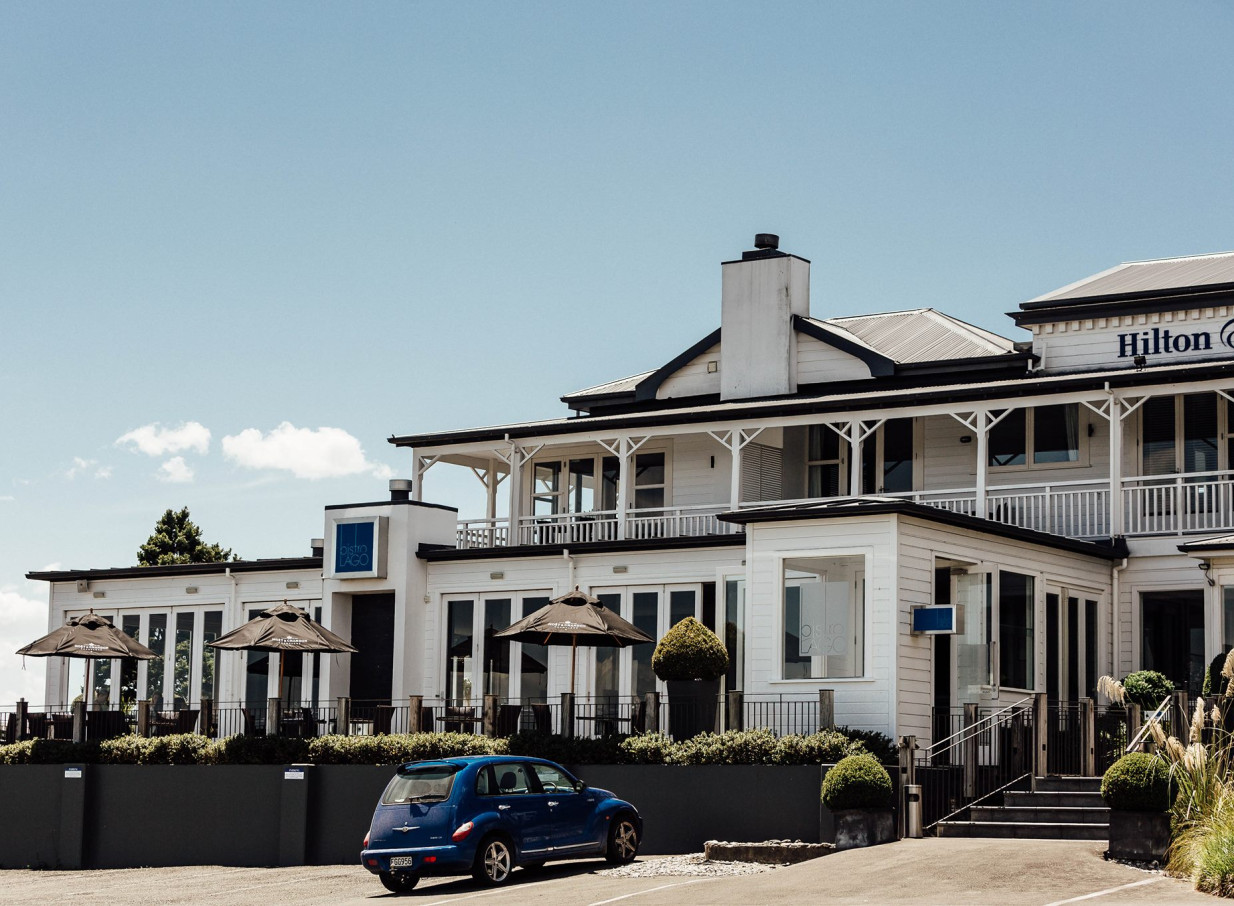 The white, Victorian-inspired heritage exterior of Hilton Lake Taupo hotel in Taupo, with an outdoor dining terrace.
