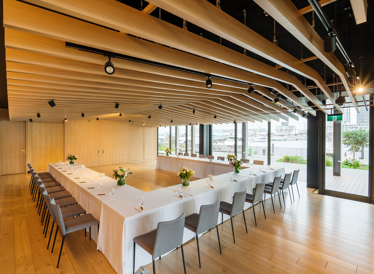 A luxurious, timber-accented meeting room at Park Hyatt Auckland, offering waterfront views and a U-shaped table setup.