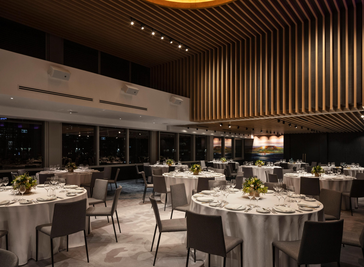 Elegant, modern event space at Park Hyatt Auckland, featuring a distinctive slatted wood ceiling and set for dining with city views.