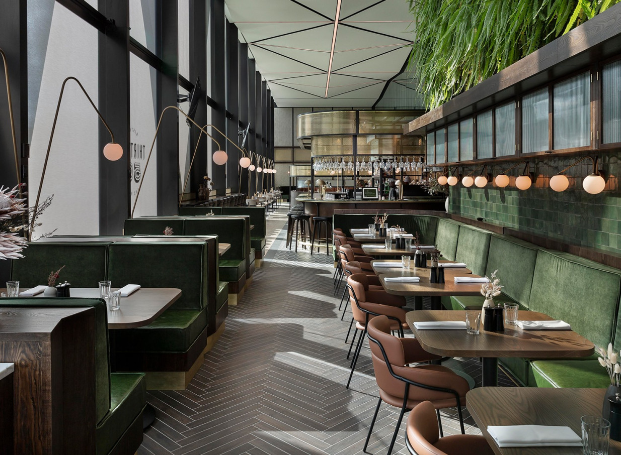 The contemporary dining area of Novotel Auckland Airport's THIRTEEN50 Bistro & Bar features green booths and a striking living green wall.