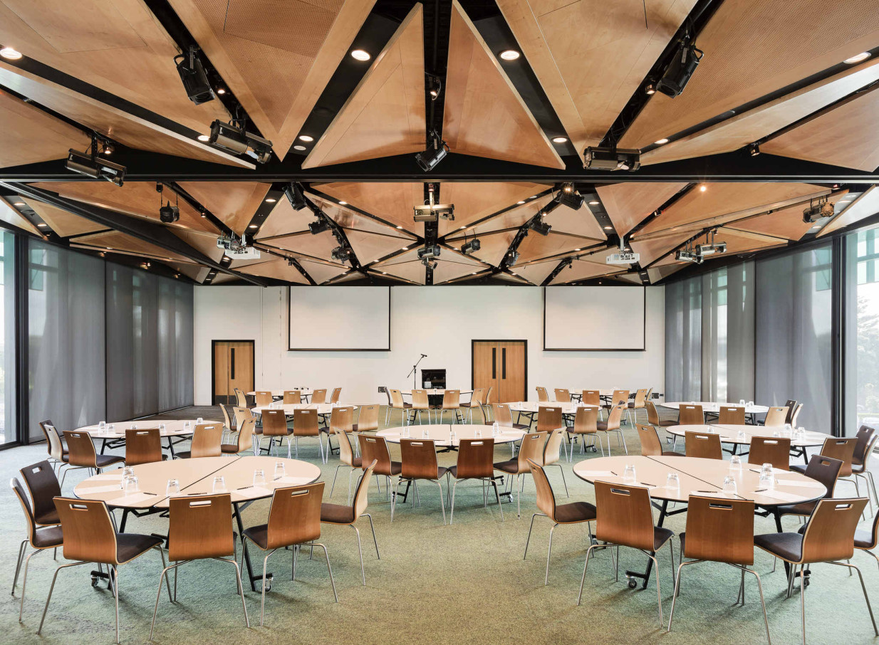 A contemporary conference room at Novotel Auckland Airport, featuring a dramatic New Zealand-inspired geometric timber ceiling and tables set for a meeting.