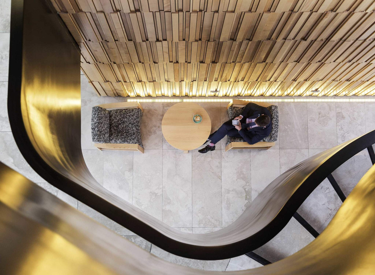 A person relaxes in the modern, New Zealand-inspired lounge of Novotel Auckland Airport, featuring unique wooden wall panels and a sculptural golden accent.