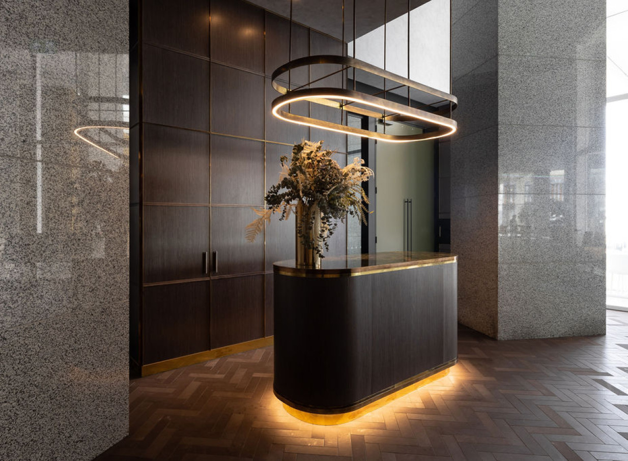 A sophisticated modern reception with dark wood, brass accents, and a distinctive oval light at Commercial Bay Meeting Suites, Auckland.