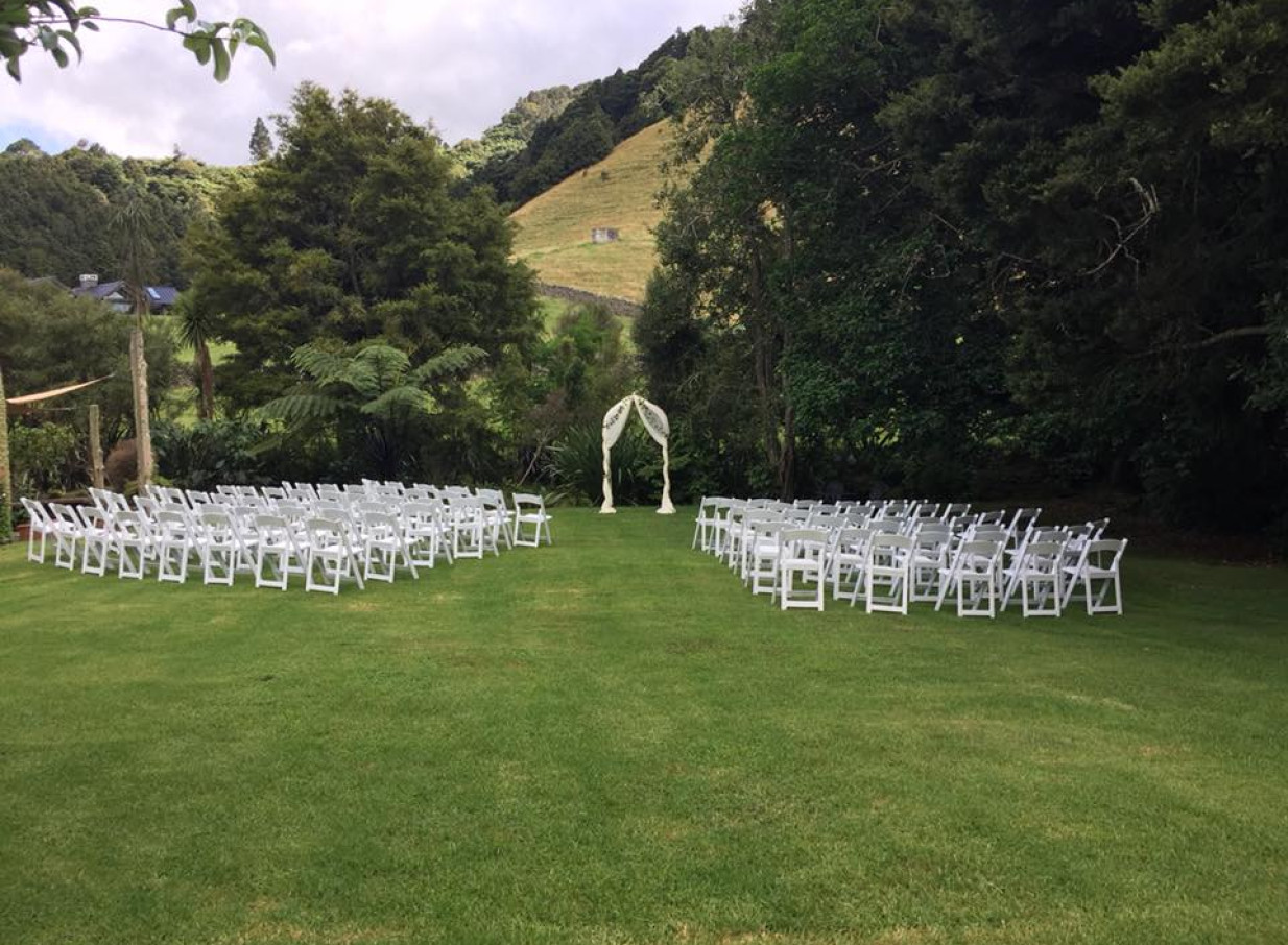 An outdoor ceremony with white chairs and arch at The James Homestead, a historic home and garden venue in Whangarei.