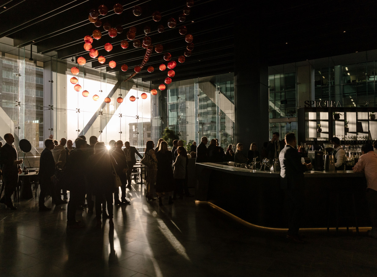 Guests gather at SPECTRA, a modern, glass-enclosed bar and event space in Auckland, featuring city views and unique lighting.
