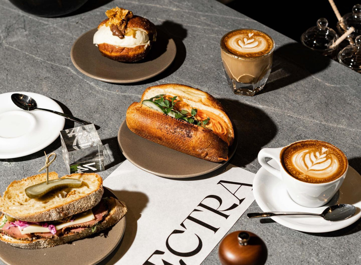 Gourmet sandwiches, a pastry, and lattes on a sleek table at SPECTRA, a contemporary cafe in Auckland.
