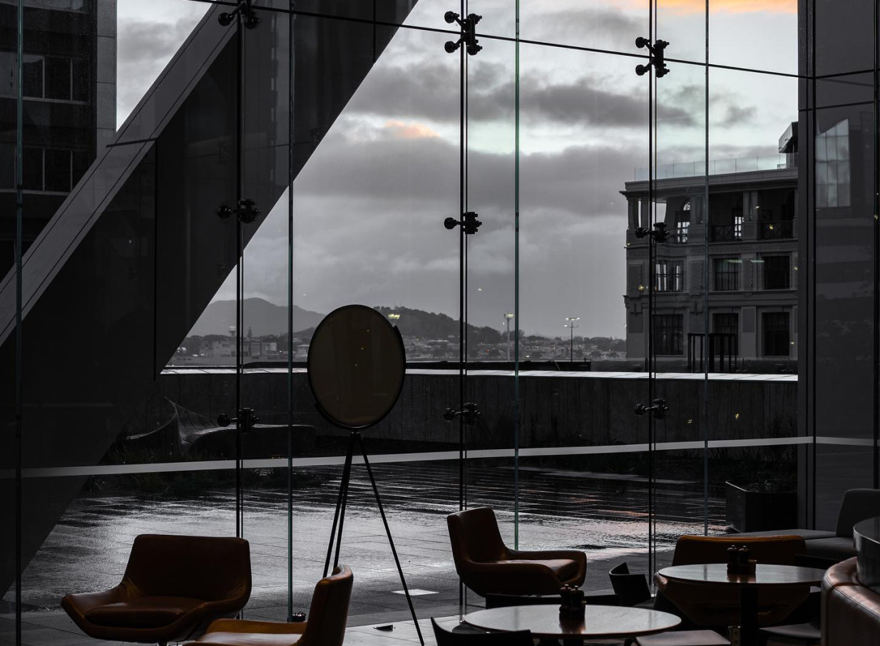 A sleek, modern lounge area with floor-to-ceiling windows at SPECTRA in Auckland, offering city views on a cloudy day.