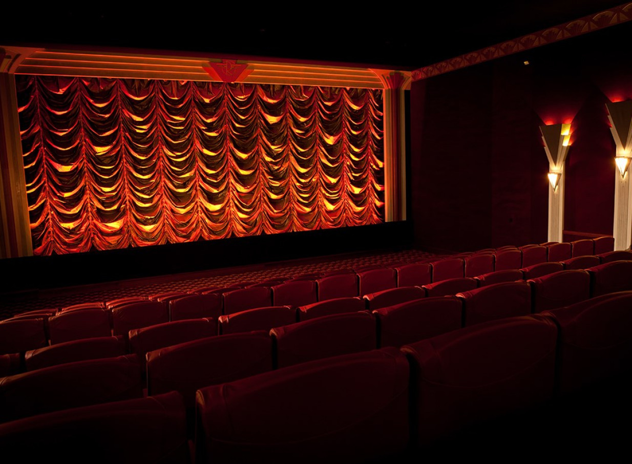 The Art Deco cinema auditorium at The Roxy in Wellington features rows of red seats facing an illuminated stage curtain.