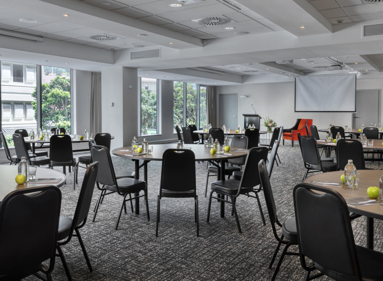 A modern conference room with natural light and round tables is set for an event at Rydges Wellington.