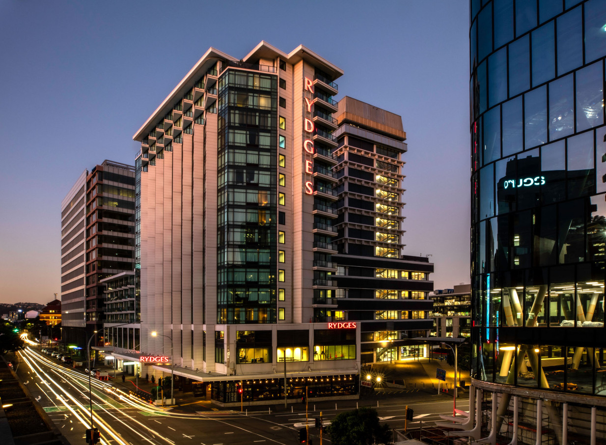 Rydges Wellington's modern slender tower with sawtooth setbacks and ribbed fins illuminates the city at dusk.