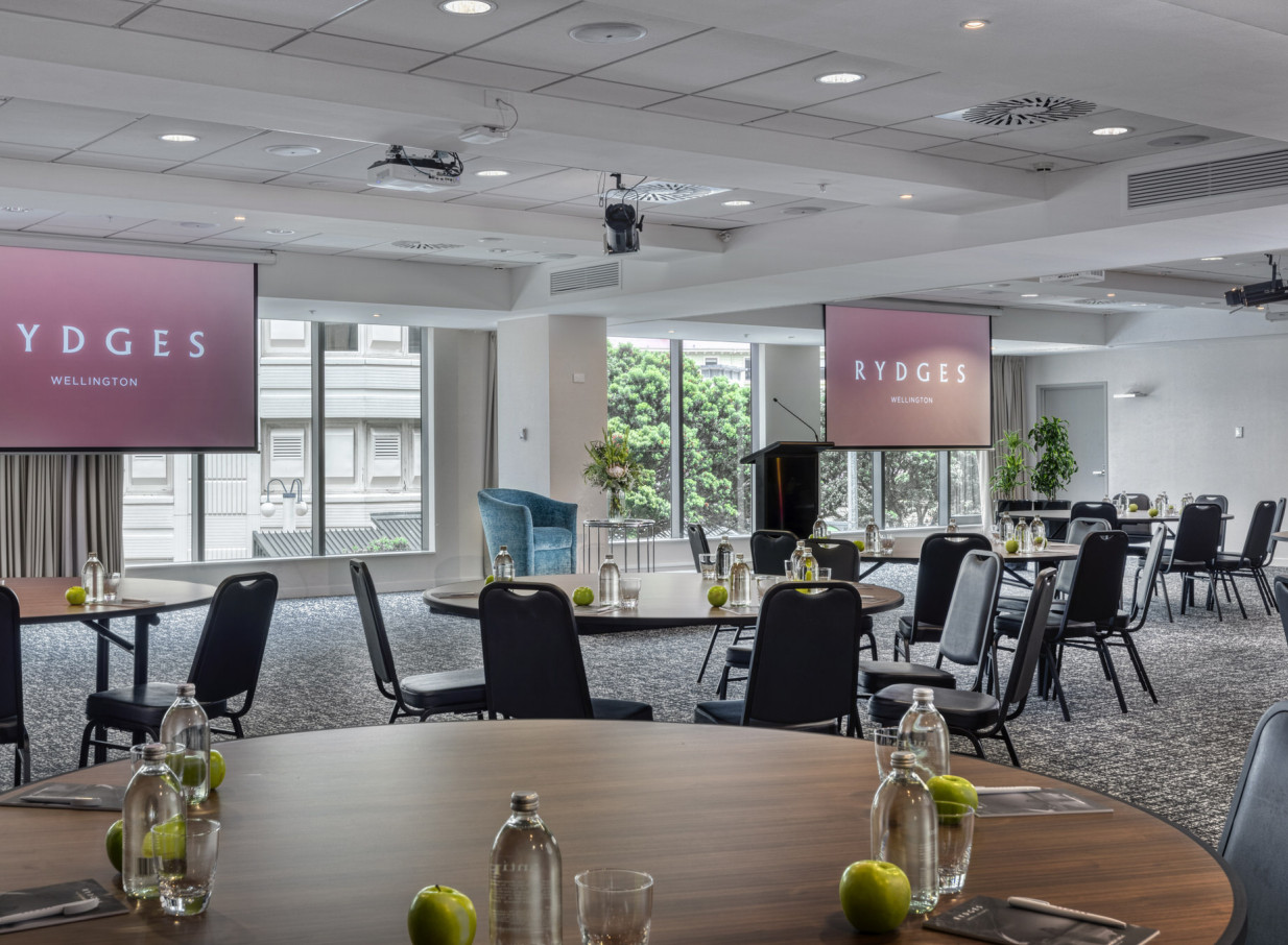 A modern, naturally lit conference room at Rydges Wellington, set with round tables and projection screens.