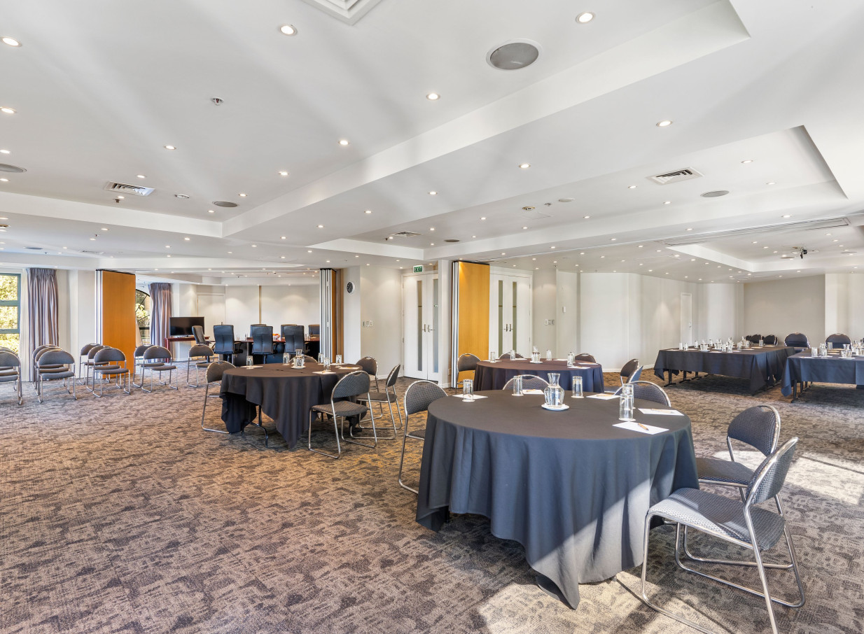 A bright, modern conference room at the Parkside Hotel and Apartments in Auckland, set with round tables and chairs for a meeting.