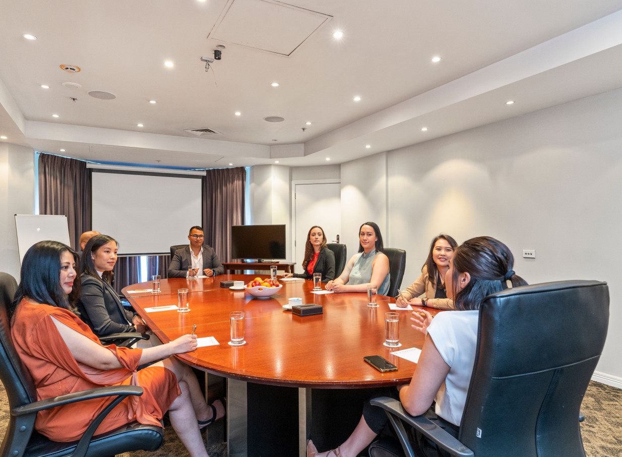 A modern conference room at Parkside Hotel and Apartments in Auckland hosts a meeting with attendees seated around an oval table.
