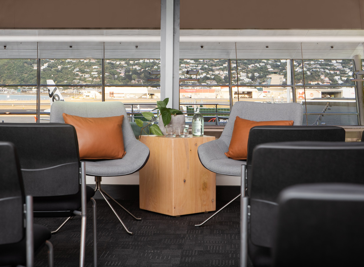 A modern, industrial-chic lounge area at Rydges Wellington Airport offers comfortable seating with a direct view of the runway.