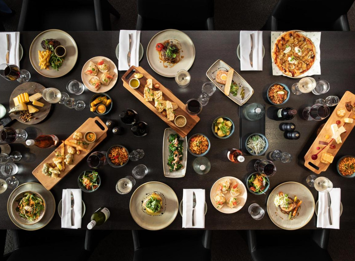 A contemporary long table dinner with diverse cuisine and drinks, embodying the modern style of Rydges Wellington Airport.