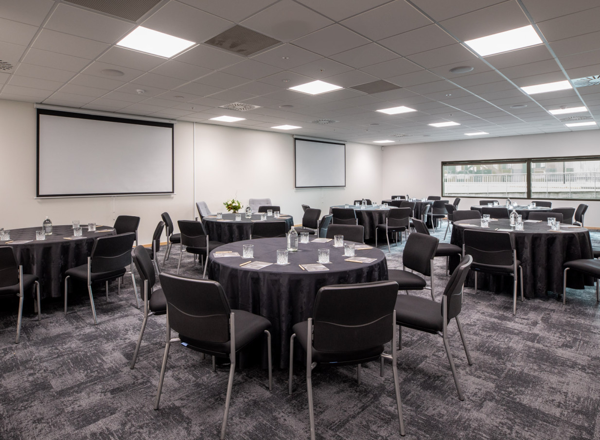 A modern meeting room setup with round tables and projectors at Rydges Wellington Airport.