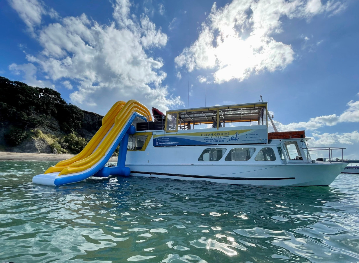 Ocean Groove Cruises in Auckland showcases its party boat with a vibrant two-storey inflatable slide into the water.