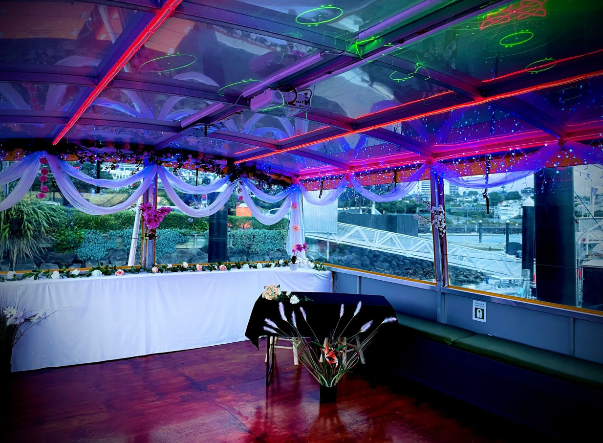 A vibrantly lit event space on an Ocean Groove Cruises party boat in Auckland, featuring festive decor under a glass roof.