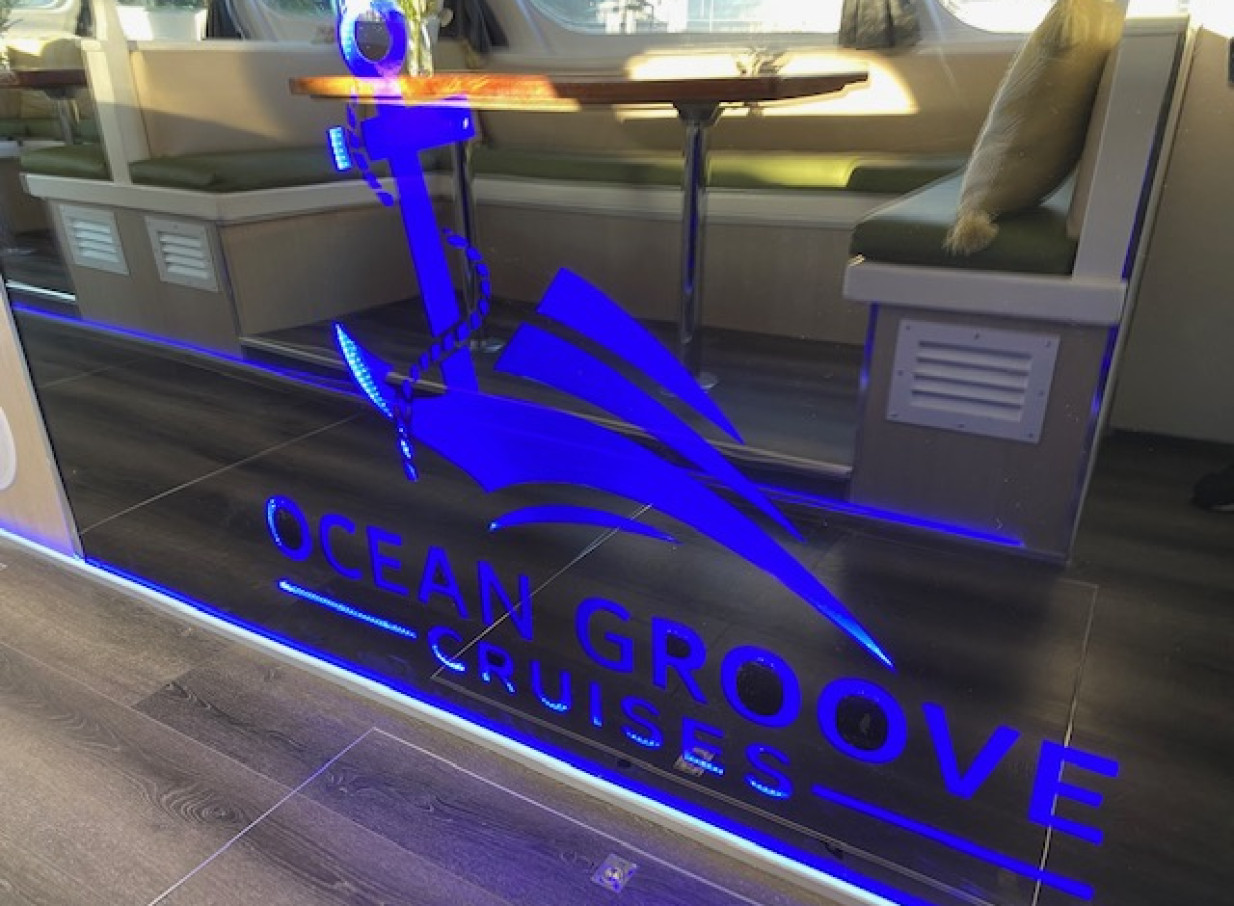 A modern, Mediterranean-inspired interior seating area on an Ocean Groove Cruises party boat in Auckland, featuring a glowing blue logo.