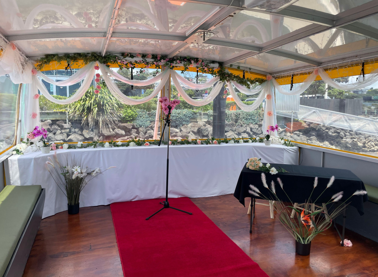 A decorated ceremony space with a red carpet and floral arrangements aboard Ocean Groove Cruises' Auckland harbour event boat.