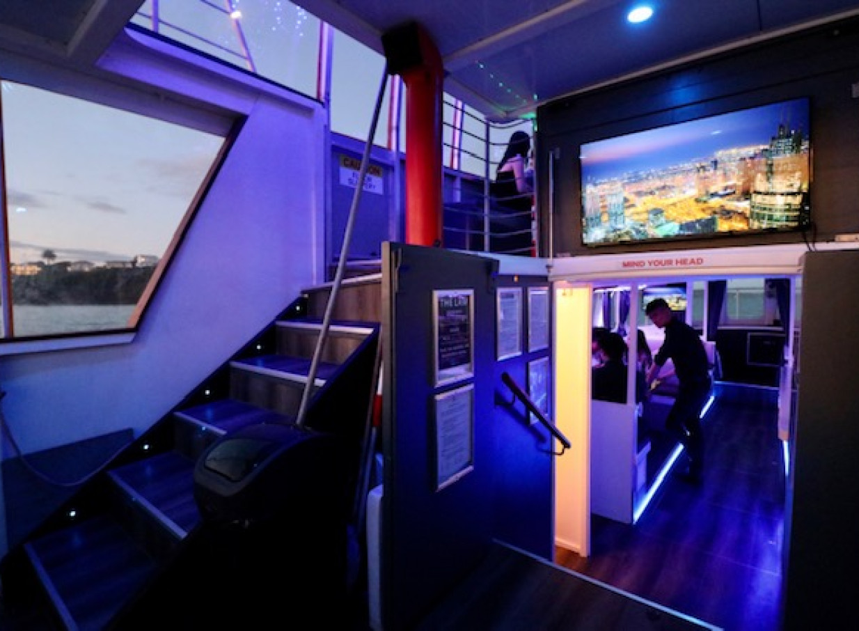A multi-level party deck with illuminated stairs and harbor views aboard the modern Ocean Groove Cruises vessel in Auckland.