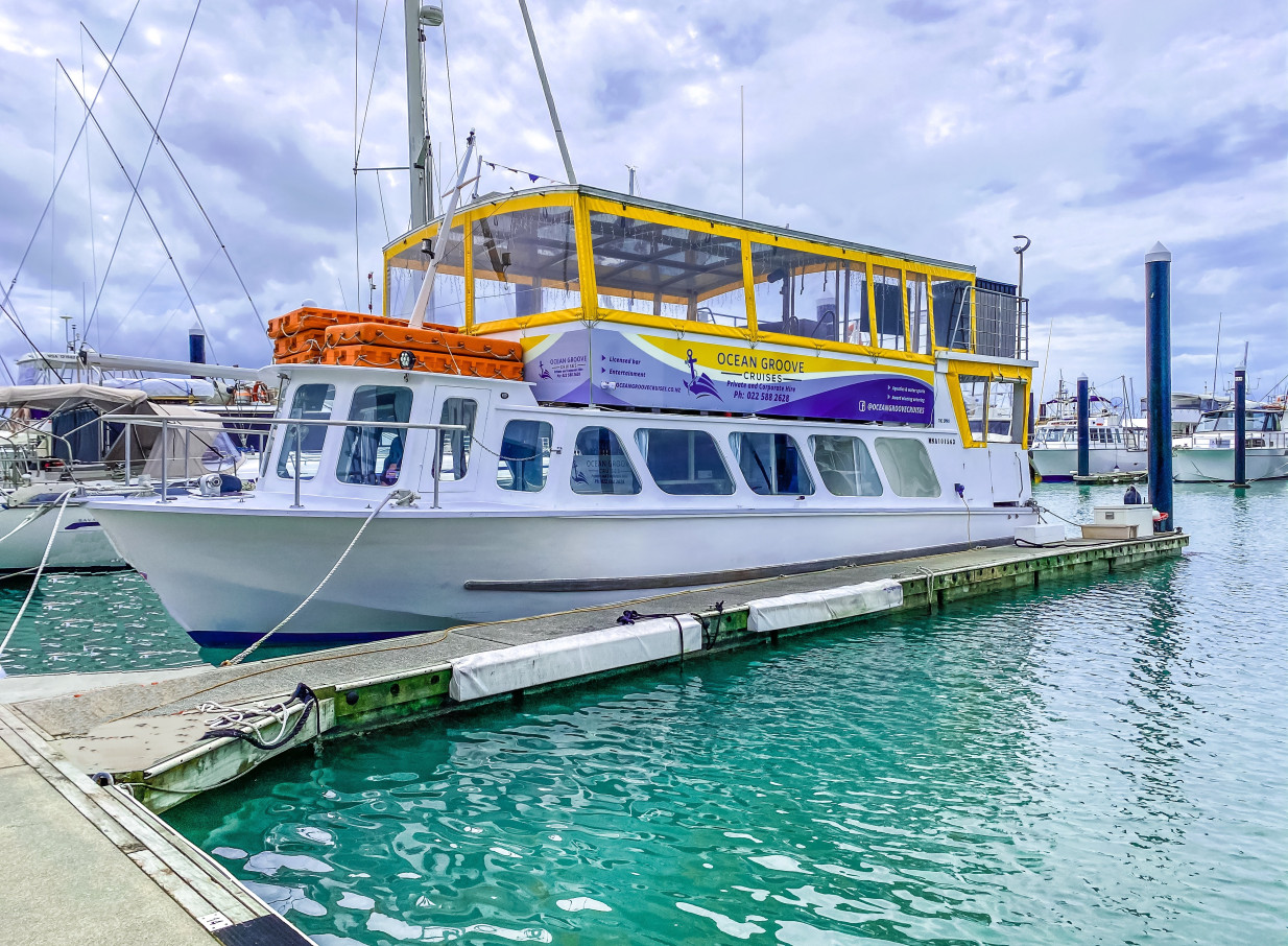 The Ocean Groove Cruises party boat, a contemporary event vessel in Auckland, is docked at a marina.