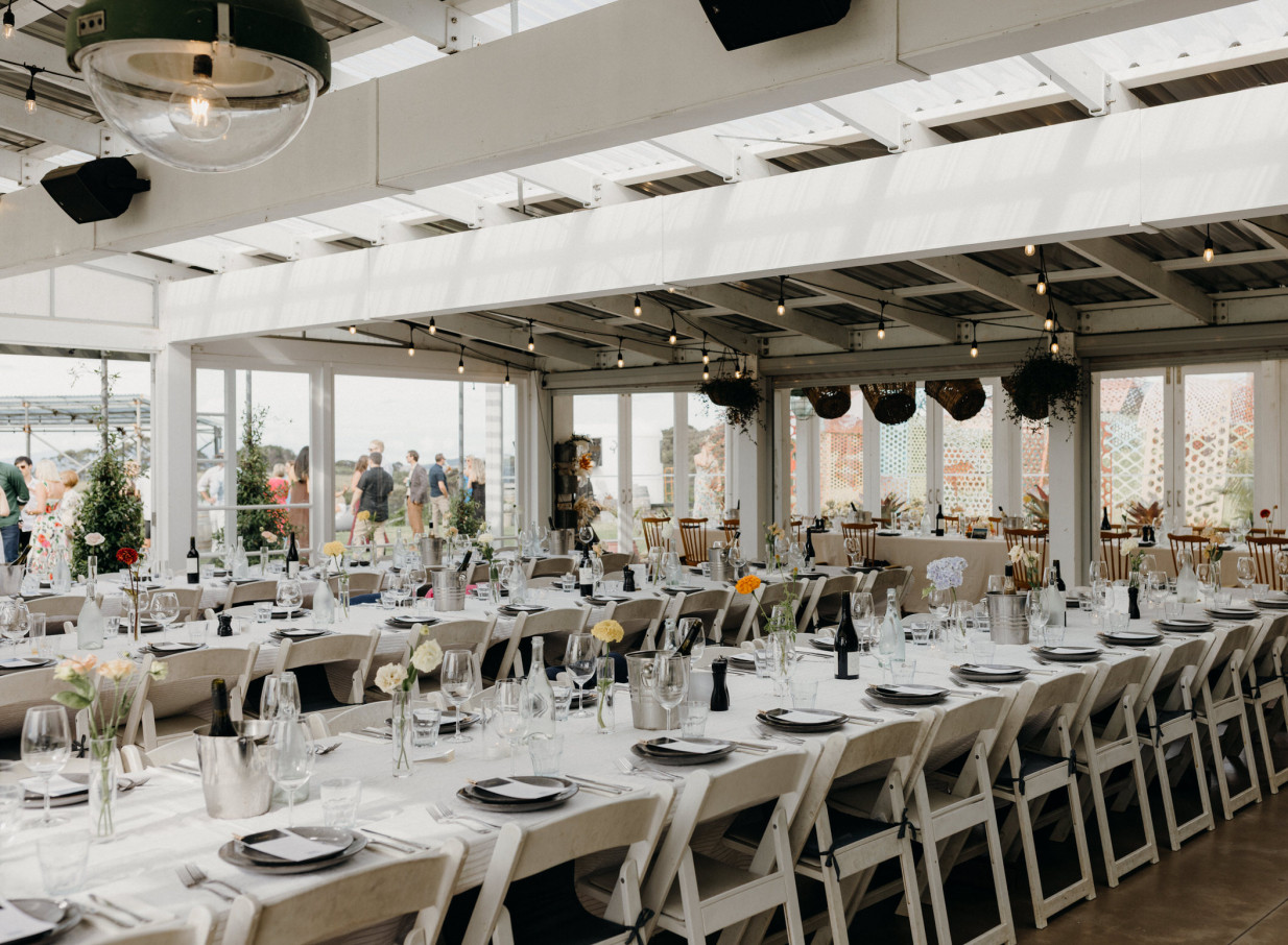A light-filled event dining space at Batch Winery's modern, all-glass Greenhouse & Terrace on Waiheke Island, offering panoramic vineyard views.