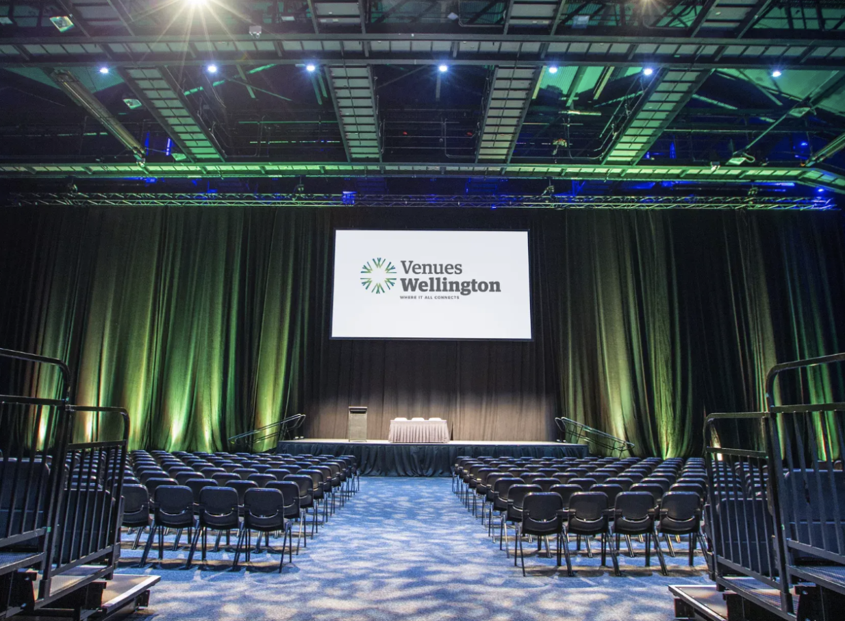 The TSB Arena, a modern multi-purpose venue in Wellington, features an indoor event setup with rows of seating, a stage, and a screen.