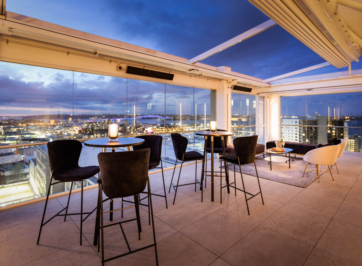 Rydges Auckland's modern rooftop bar and lounge offers a sophisticated ambiance with panoramic city and harbor views at dusk.