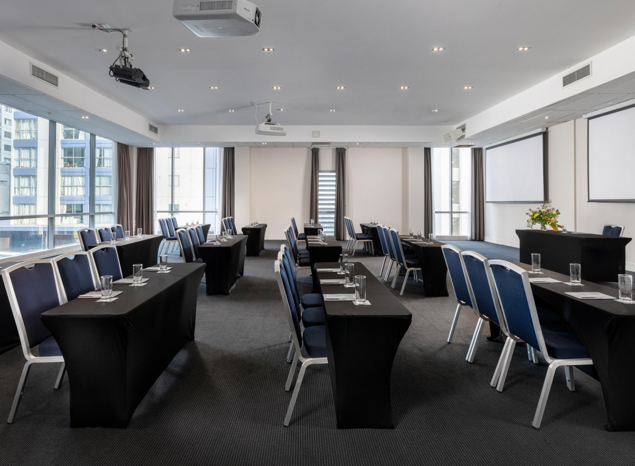 A modern conference room with natural light and floor-to-ceiling windows at Rydges Auckland, set up for a presentation.