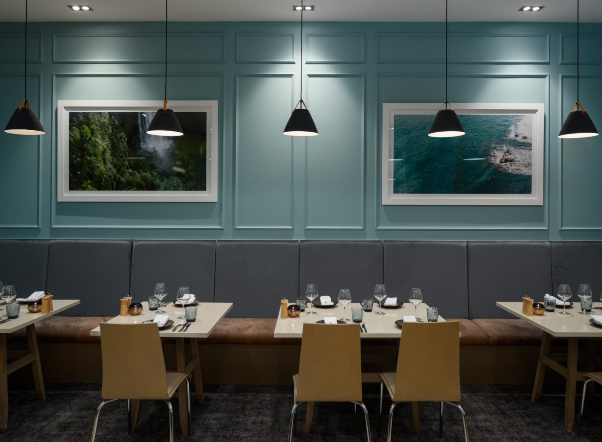 Rydges Auckland's contemporary dining room features elegant banquette seating, pendant lights, and scenic artwork on teal paneled walls.